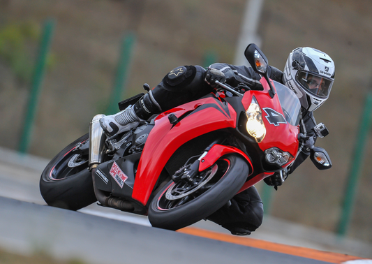 A red motorcycle is leaning in a corner on the road using a countersteering technique