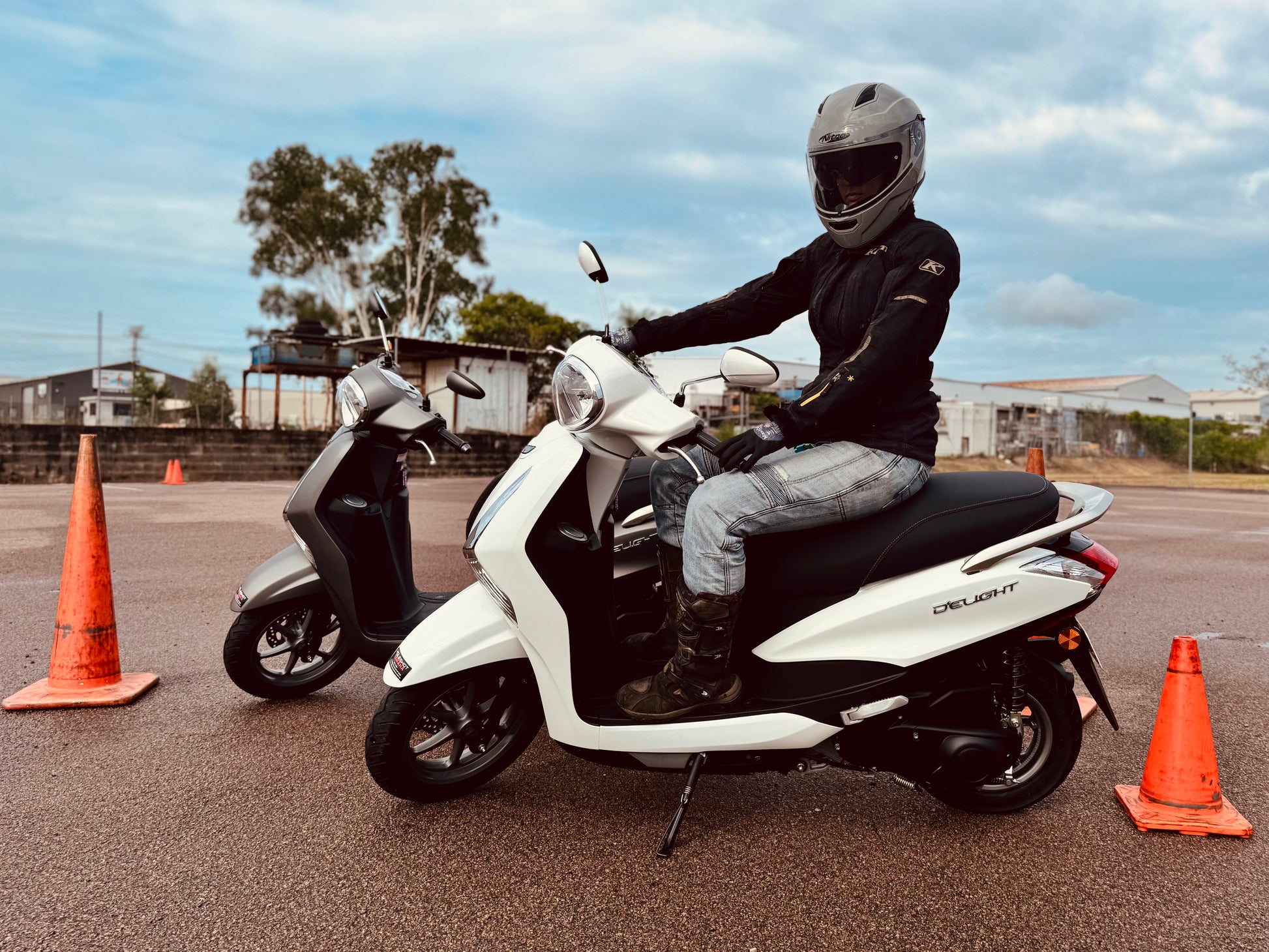 Person on a white scooter in Darwin with orange traffic cones in an open area, getting their scooter licence.