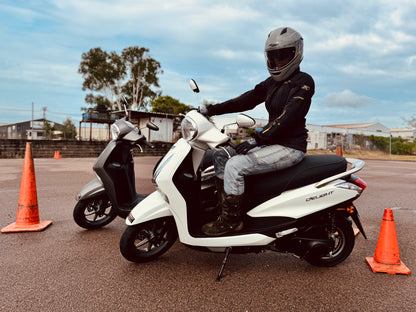 Person on a white scooter in Darwin with orange traffic cones in an open area, getting their scooter licence.