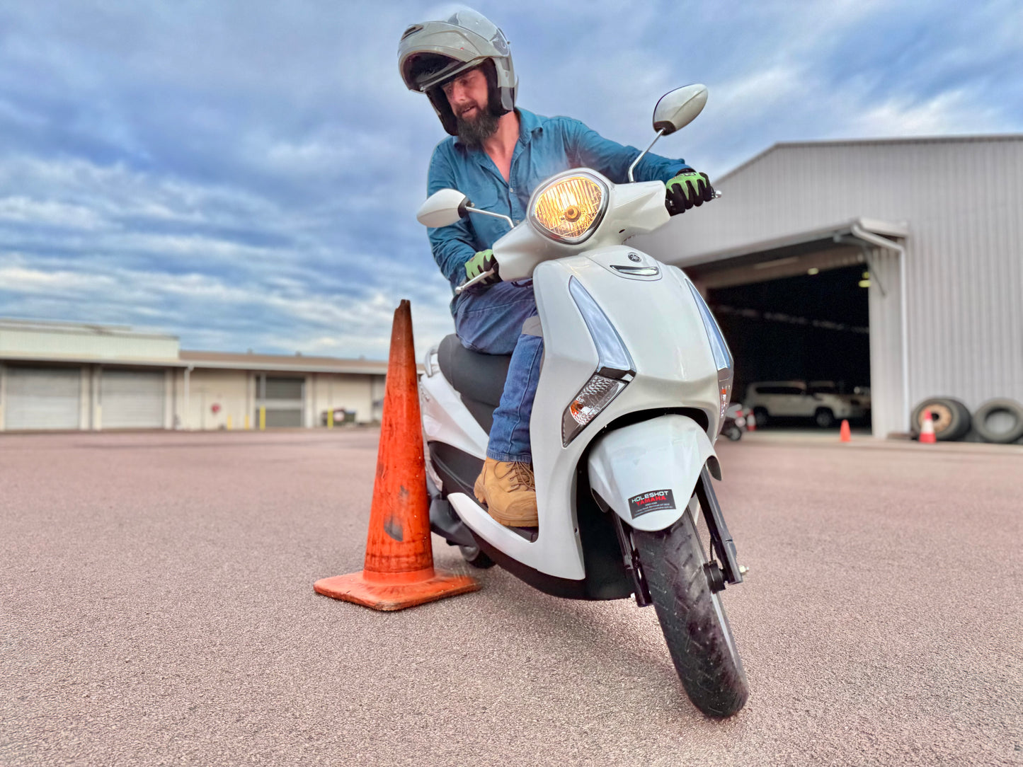 Person on a scooter next to an orange cone with a building in the background, getting a scooter licence in Darwin.