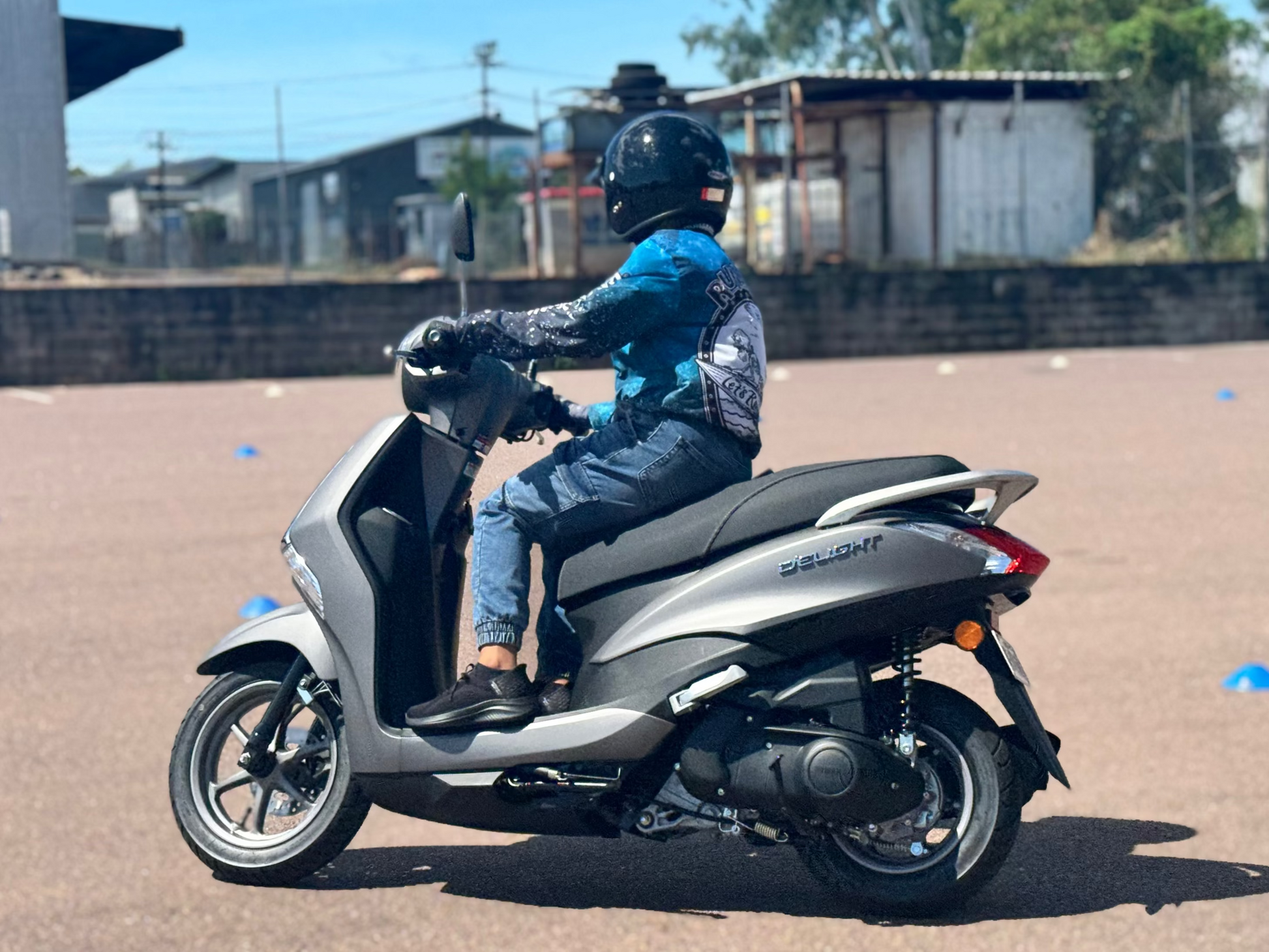 Person riding a scooter in Darwin in an open area with buildings and trees in the background